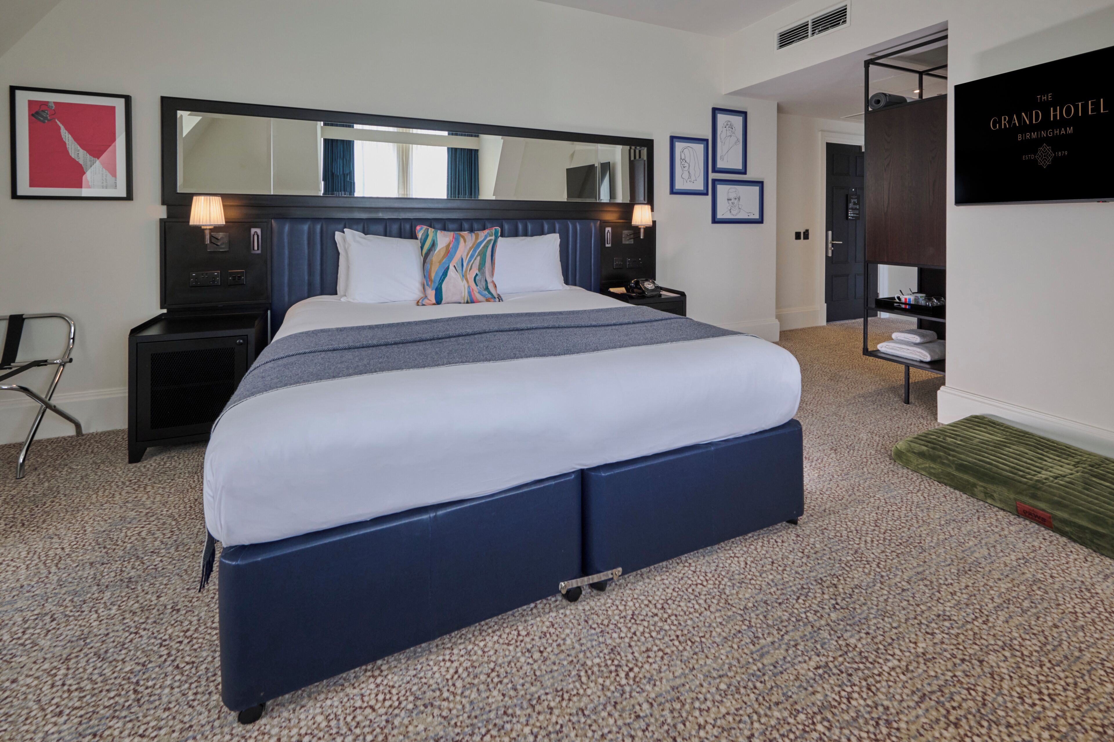 Une chambre d’hôtel avec un grand lit, un bureau, une chaise, un miroir et une armoire.