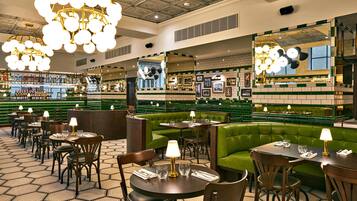 Restaurante com assentos em verde, mesas redondas e lustres pendentes.