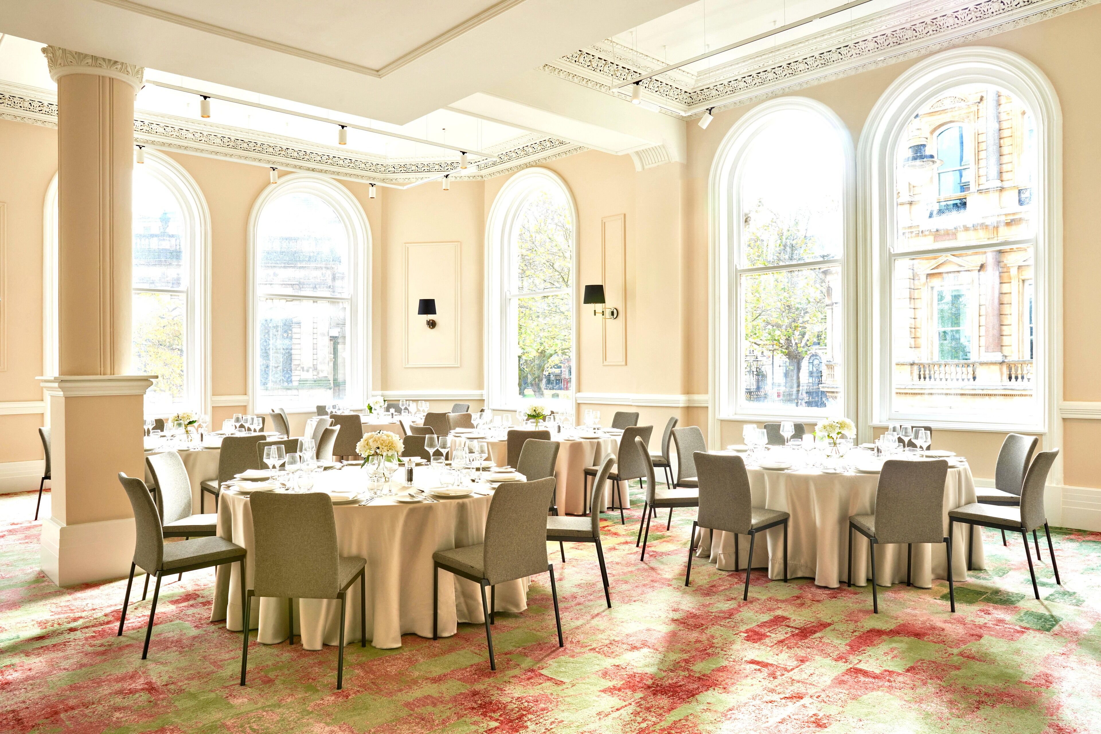 A spacious banquet hall with large windows, elegant chandeliers, and a classic architectural design.