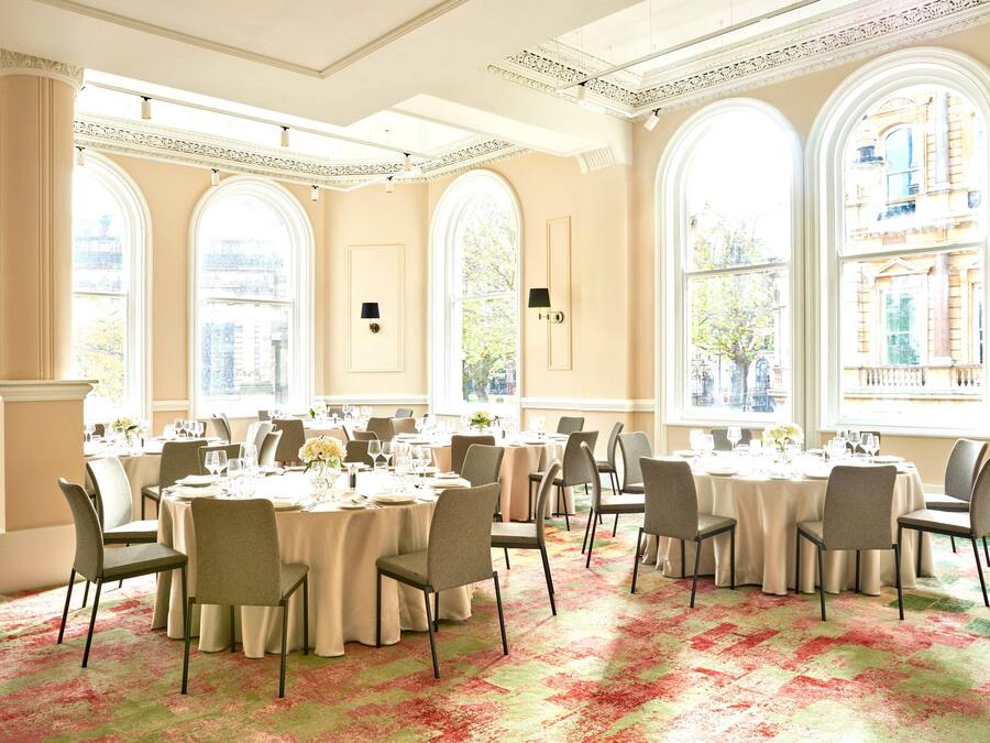 A spacious banquet hall with large windows, elegant chandeliers, and a classic architectural design.