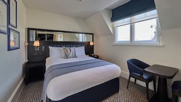 Habitación de hotel con una cama grande, un escritorio, una silla, una ventana con vistas y un cabecero con espejo y lámparas.