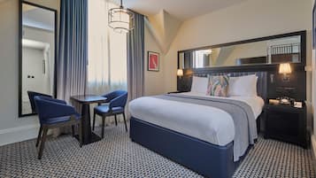 A hotel room with a large bed, two chairs, a small table, a mirror, and a nightstand with a lamp.