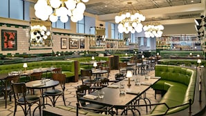 A restaurant with green booths, wooden tables, and hanging chandeliers.