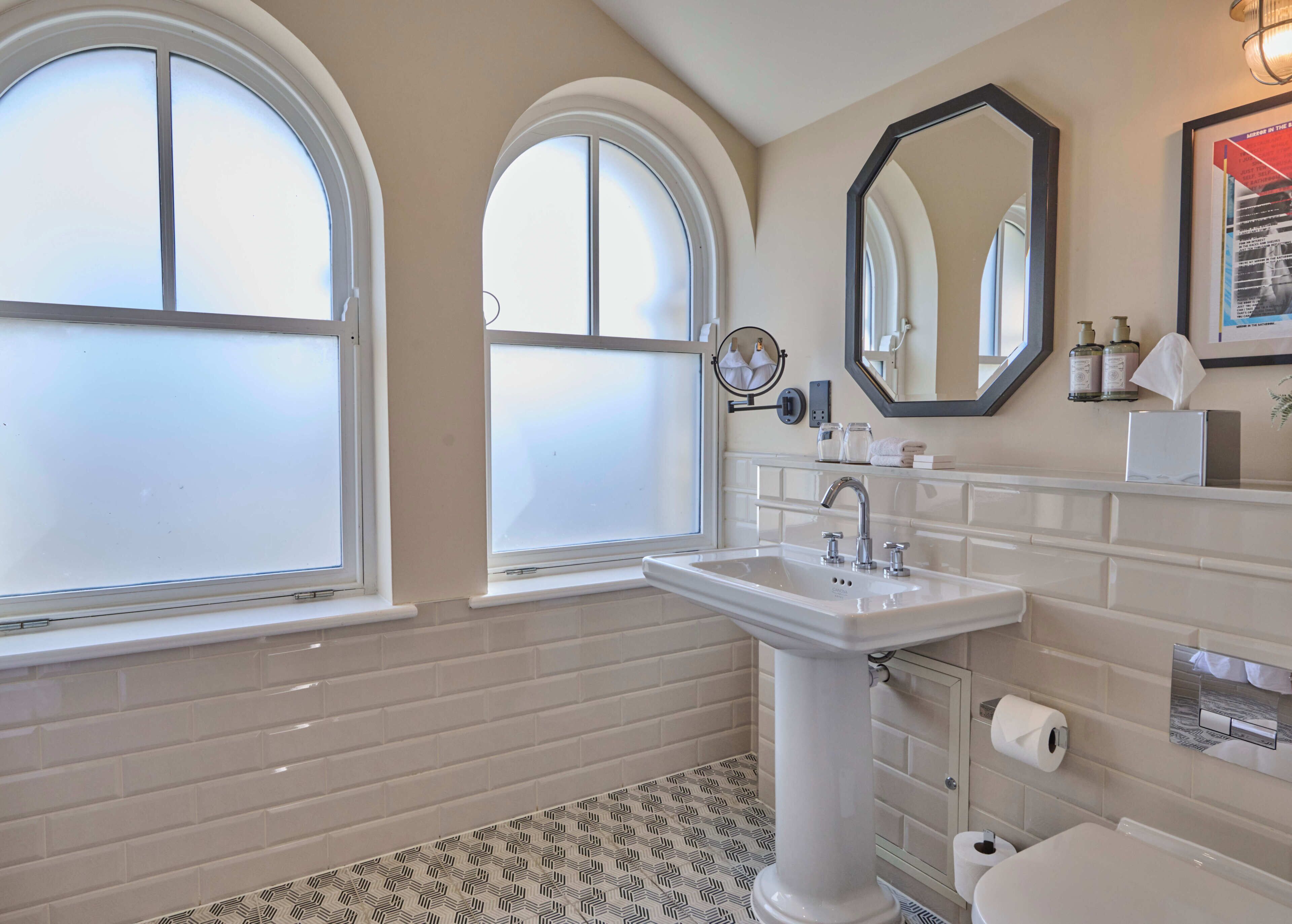 A bathroom with a white sink, a mirror, and two windows.