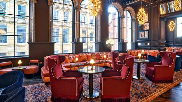 A luxurious lounge with red upholstered seating, large windows, and ornate chandeliers.