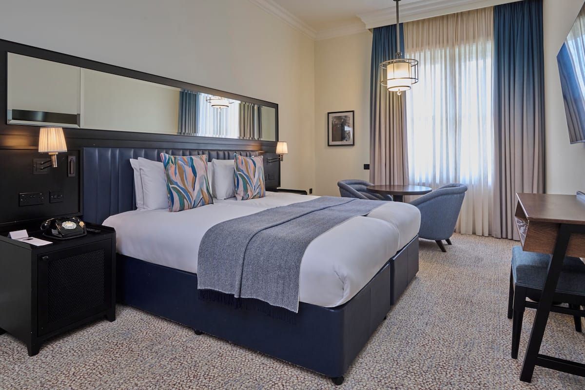 Une chambre d’hôtel avec un grand lit, un bureau, une chaise, une lampe, un téléphone et un miroir.
