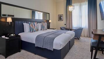 A hotel room with a large bed, a desk, a chair, a lamp, a telephone, and a mirror.