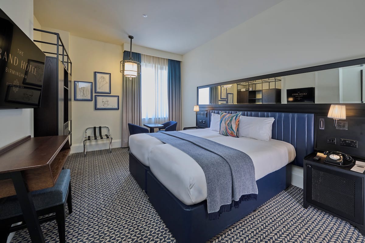 Une chambre d’hôtel avec un lit, un bureau, une chaise et un grand miroir.