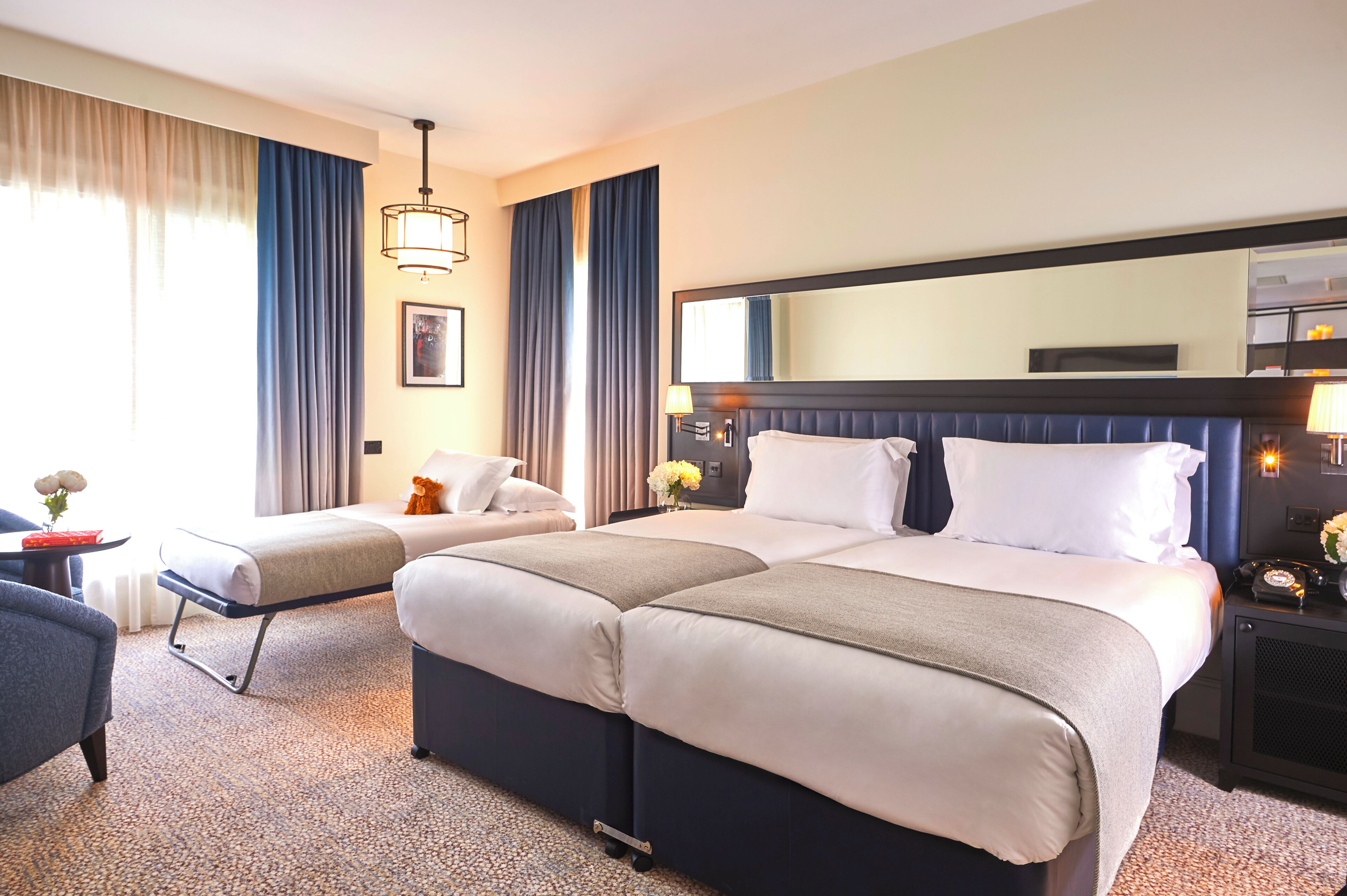 A hotel room with a large bed, a bedside table, a chair, and a large mirror.