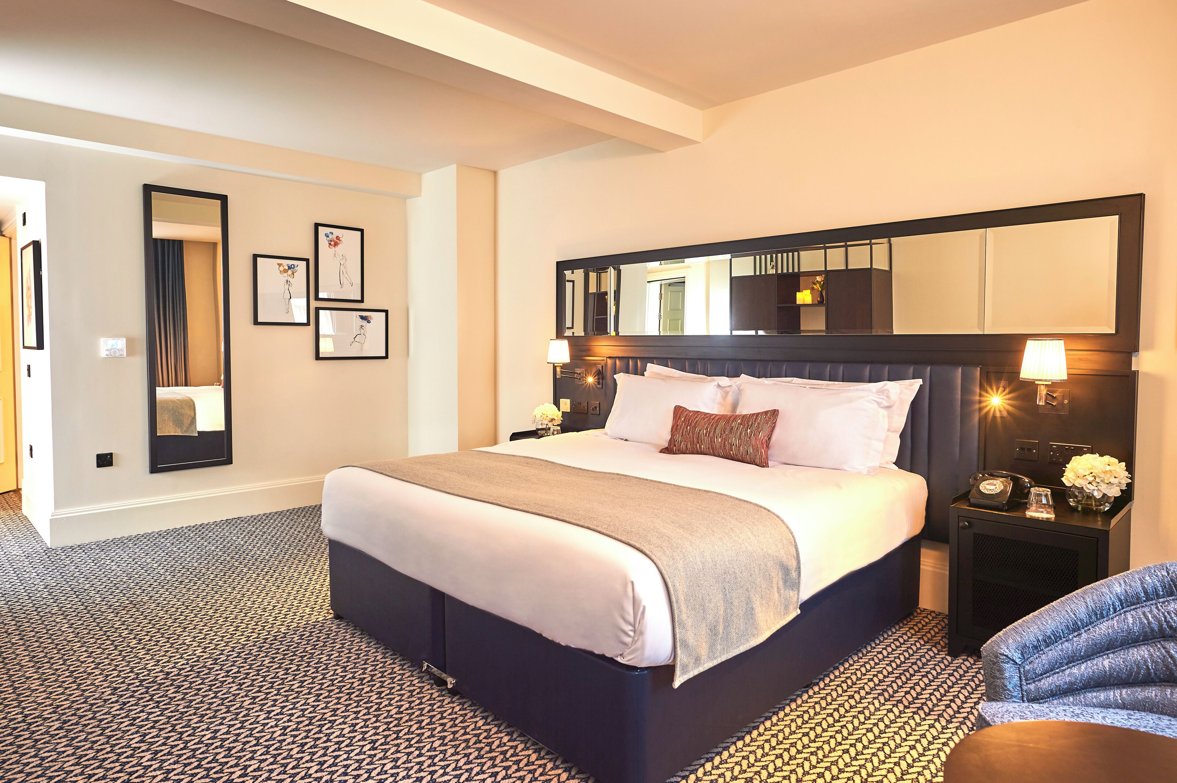 A hotel room with a large bed, a headboard mirror, bedside lamps, and a patterned carpet.
