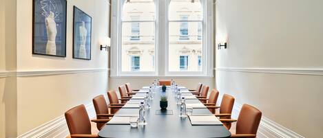 A conference room with a long table, brown chairs, and a view of buildings through large windows.
