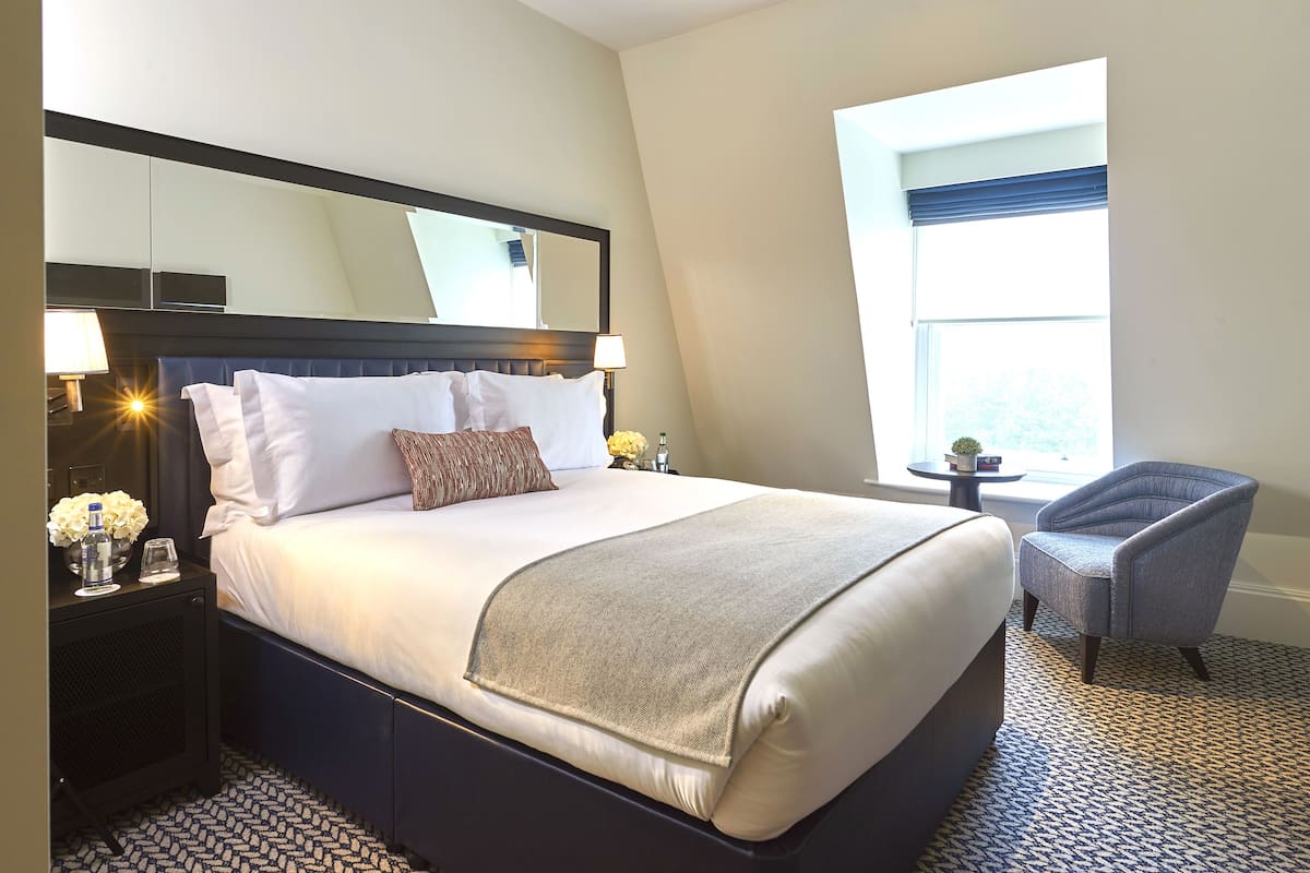 Une chambre d’hôtel avec un grand lit, une chaise, une petite table et une fenêtre.