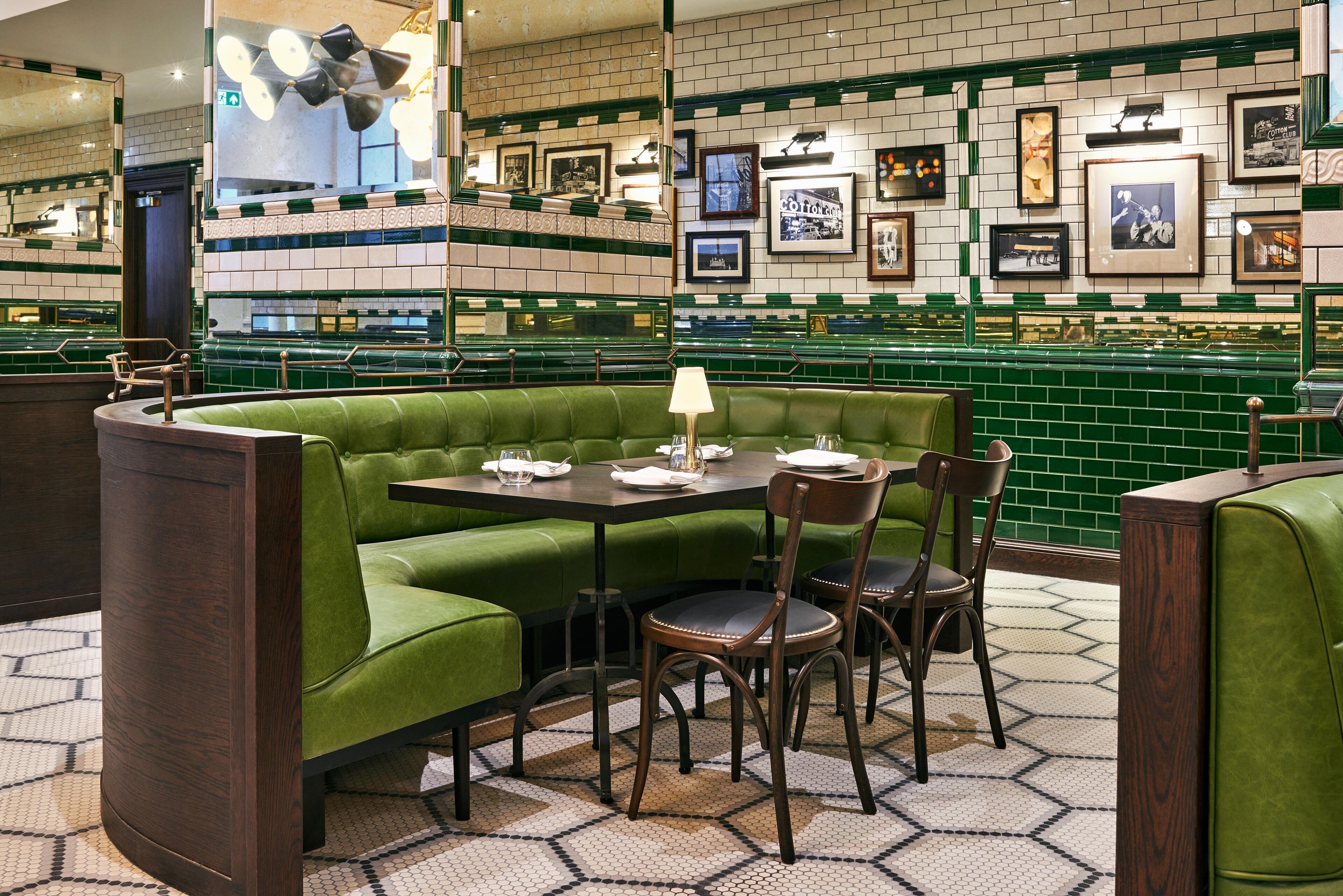 A restaurant with green booths, wooden tables, and chairs. There are framed pictures on the walls and a patterned floor.