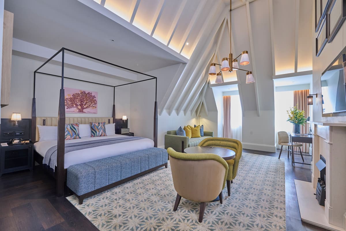 Une chambre d’hôtel moderne avec un lit à baldaquin, un coin repas comprenant une table et des chaises, et une grande fenêtre offrant une vue dégagée.