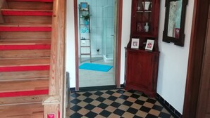 Een trap met rode treden die leidt naar een hal met een zwart-wit betegelde vloer, een houten kast met ingelijste foto's, en een blauwe mat bij de ingang.