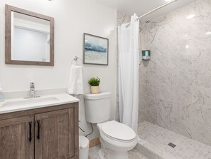 Ein modernes Badezimmer mit einer Marmerdusche, einer Toilette, einem Waschbecken mit Spiegel und einem gerahmten Bild an der Wand.
