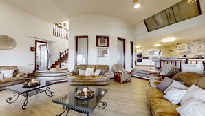 A spacious living room with a staircase, a kitchen in the background, and a dining area.