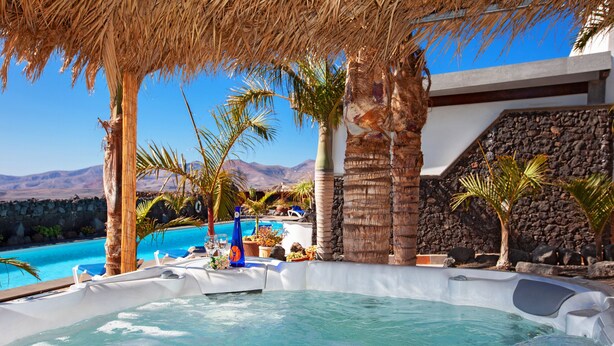 A hot tub area with a pool, palm trees, and a stone wall.