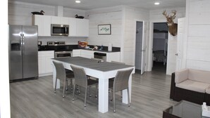 A modern kitchen with white cabinetry, stainless steel appliances, and a dining area with wicker chairs. - Venice Blue Crab Lodge A (Waterfront) (Venice)