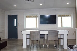 A room with a dining table, chairs, a TV mounted on the wall, and a door.