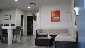 A modern living room with a sofa, a coffee table, a dining table with chairs, and a wall-mounted deer head. - Venice Blue Crab Lodge A (Waterfront) (Venice)