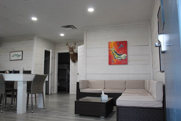 A modern living room with a sofa, a coffee table, a dining table with chairs, and a wall-mounted deer head.