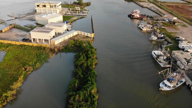 A marina with boats docked, a building with a flat roof, and a river. - Venice Blue Crab Lodge A (Waterfront) (Venice)