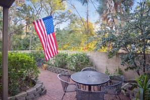 An outdoor patio with a table and chairs, surrounded by a stone wall and lush greenery.