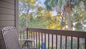 A porch with a chair and an American flag, overlooking a garden with various trees and plants. - Hilton Head Beach Club - 3 Bedroom w/ a Private Patio! (Hilton Head Island)