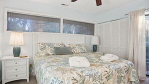 A bedroom with a bed, two bedside tables, a ceiling fan, a window with blinds, and a door with a curtain. - Hilton Head Beach Club - 3 Bedroom w/ a Private Patio! (Hilton Head Island)