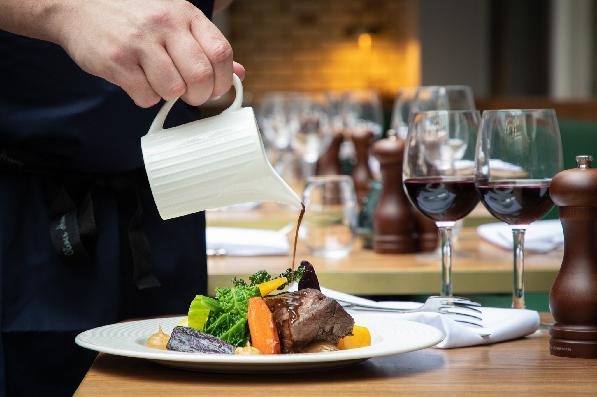 A person pouring sauce over a dish with vegetables and meat.