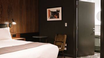 Een hotelkamer met een bed, een stoel, een tafeltje en een aan de muur hangend schilderij.