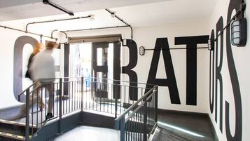 A hallway with large black letters spelling "HOTEL" on the wall, metal railings, and a door leading to another room.