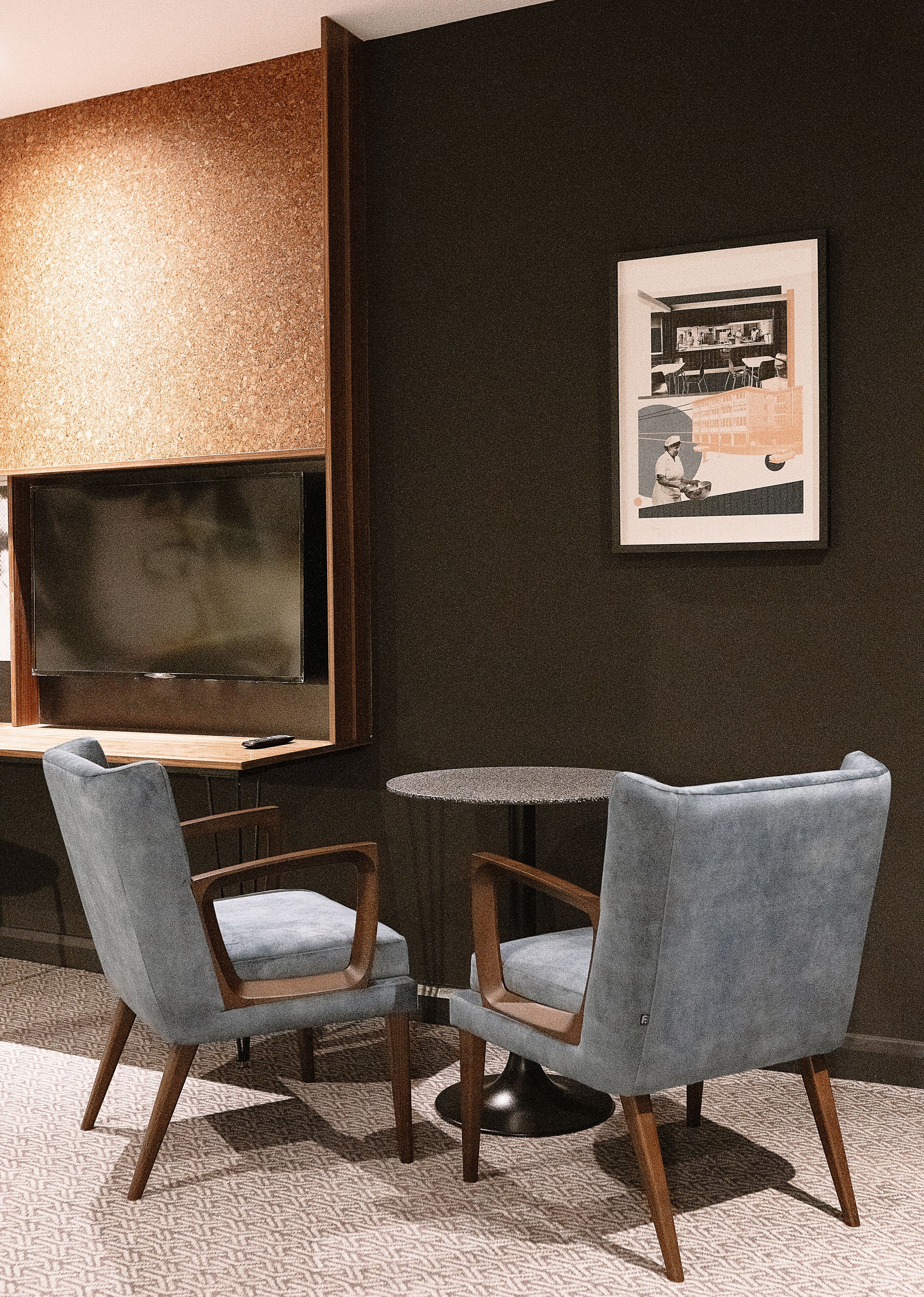 A modern room with a dark wall, a framed picture, a round table, two chairs, and a flat-screen TV.