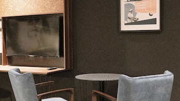 Una habitación moderna con una pared oscura, un cuadro enmarcado, una mesa redonda, dos sillas y un televisor de pantalla plana.