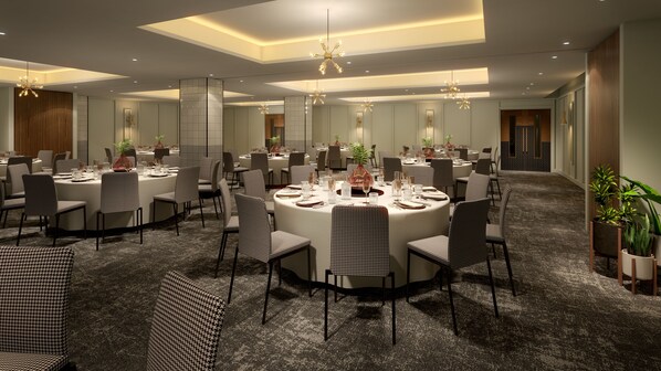 A spacious conference room with round tables, black and white checkered chairs, and modern chandeliers.