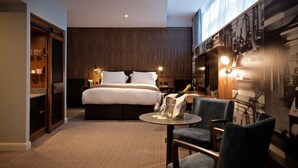 A hotel room with a large bed, a small round table with a bottle and glasses, a chair, and a minibar. - Telegraph Hotel - Coventry (Coventry)