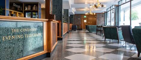 A hotel lobby with a checkered floor, a reception desk labeled "The Coventry Evening Telegraph," and a bar area with shelves.