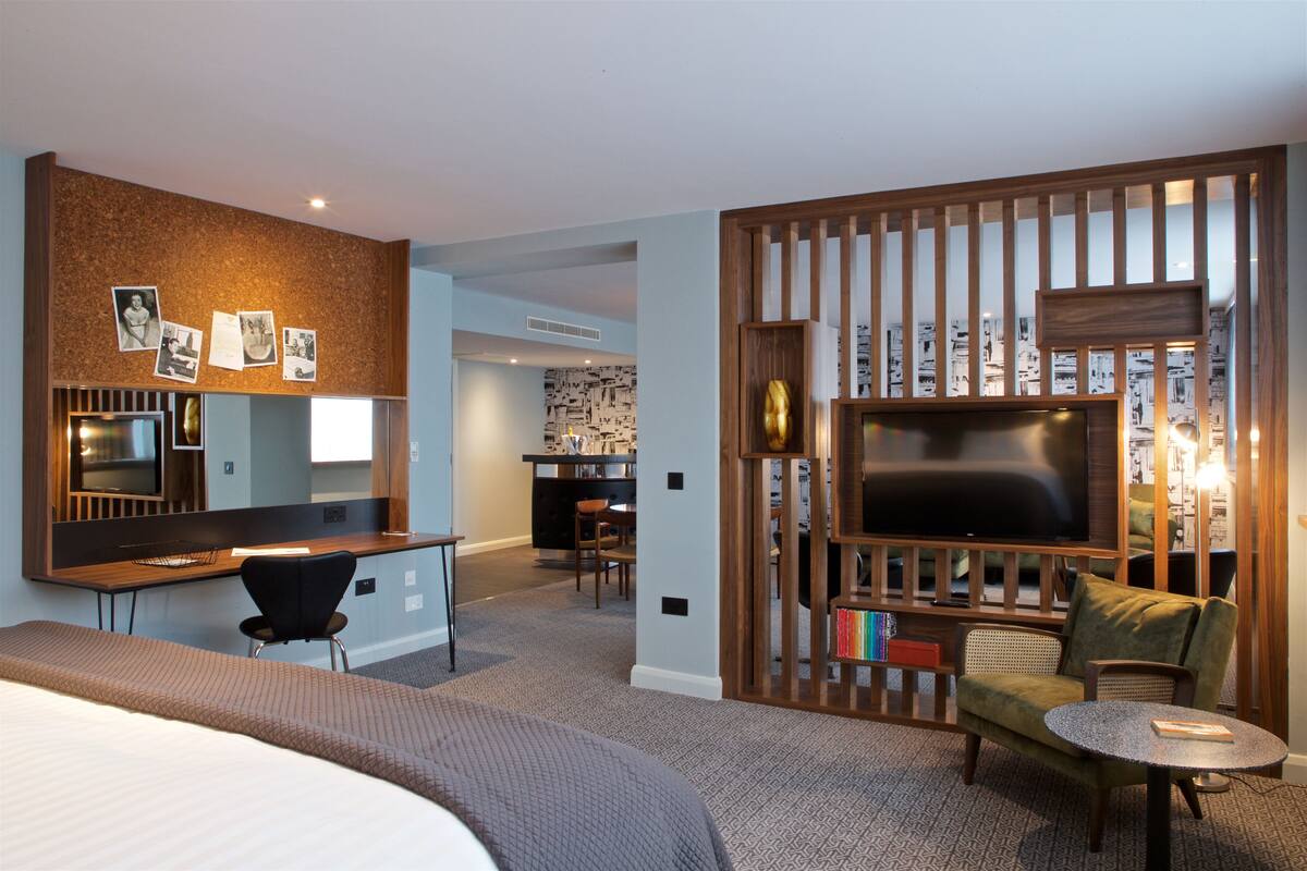 A hotel room with a bed, a desk, a TV, and a seating area with a chair and a small table.