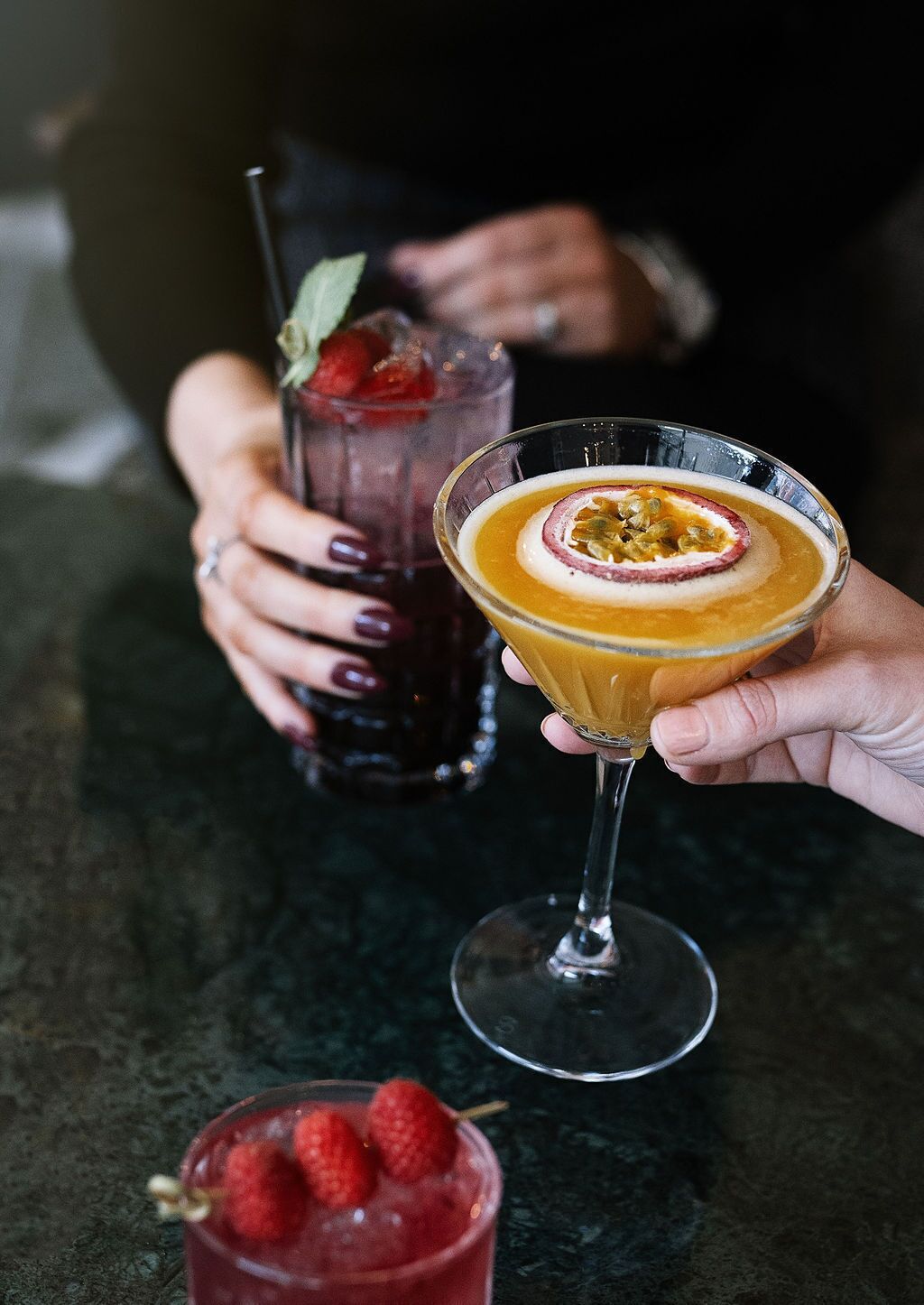 Zwei Cocktails in Martini-Gläsern, einer mit Obstgarnitur und der andere mit einer Marakujenscheibe.