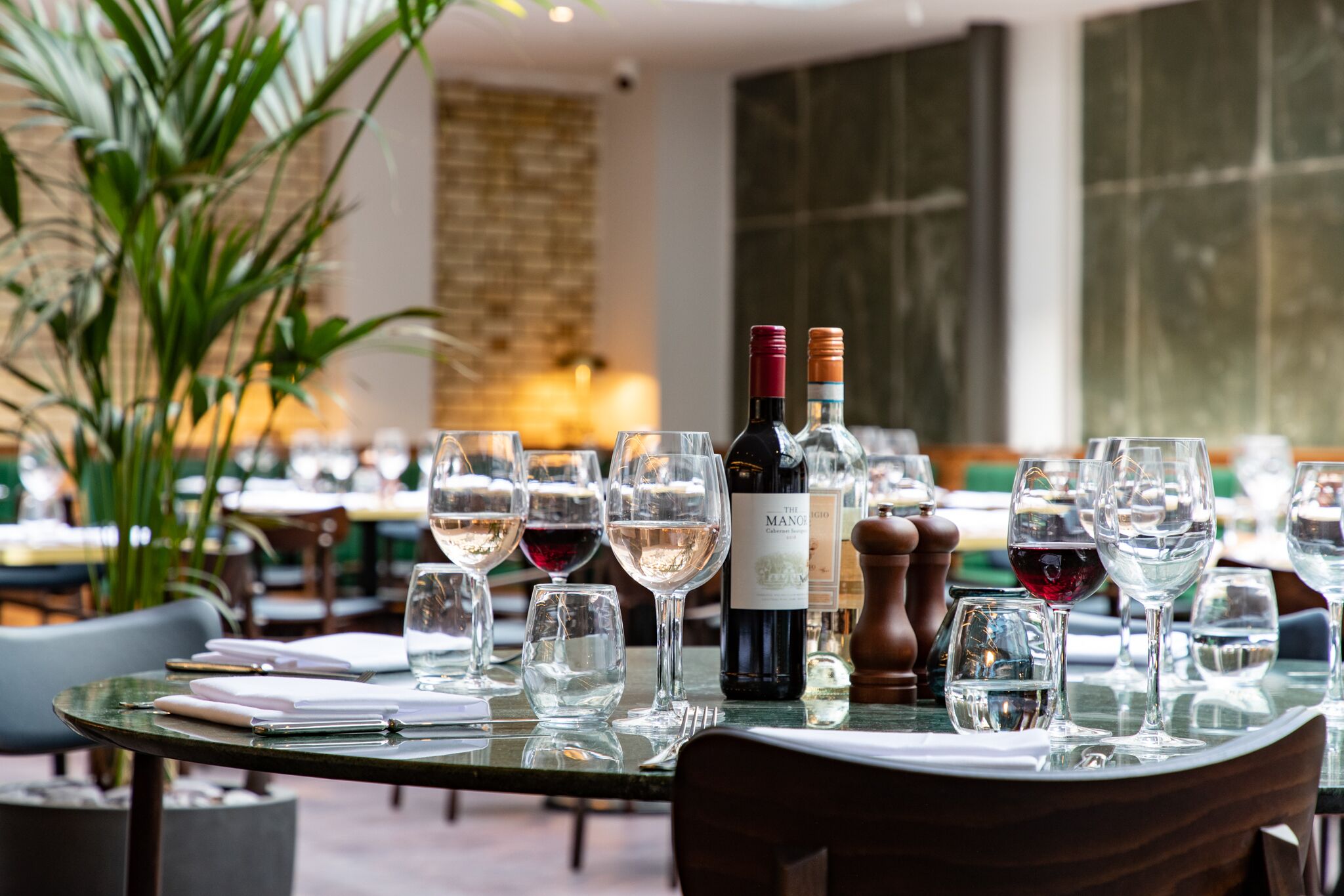 Mesa de restaurante preparada con copas de vino, una botella de vino y salero y pimentero.