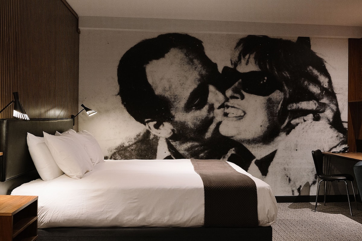 A hotel room with a large bed, a desk, and a wall mural.