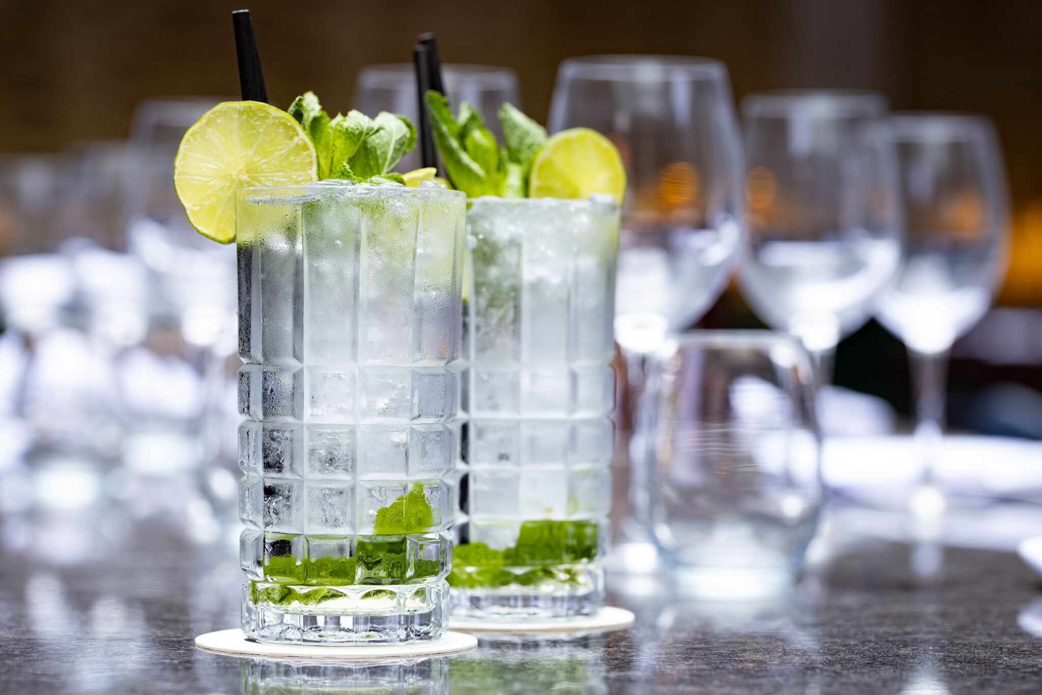 Two tall glasses of a clear beverage with ice cubes, garnished with lime and mint leaves.