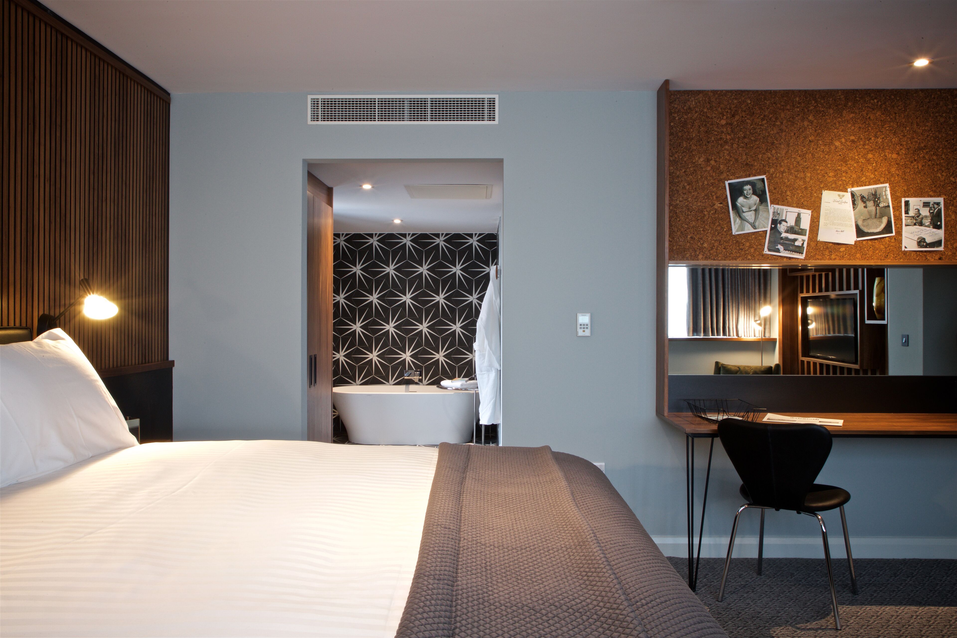 Habitación de hotel con cama, escritorio, silla, baño y una pared con cuadros.