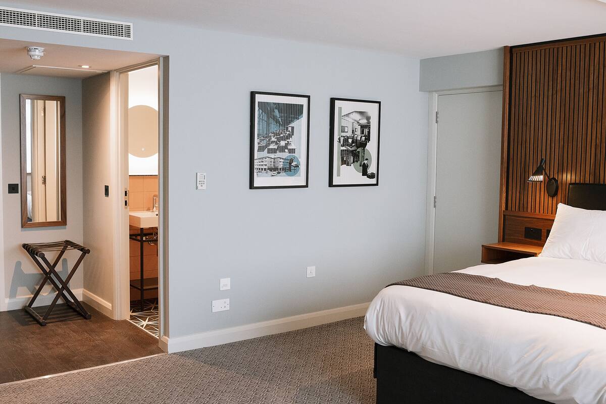 A hotel room with a bed, a wooden headboard, a nightstand, a mirror, and two framed pictures on the wall.