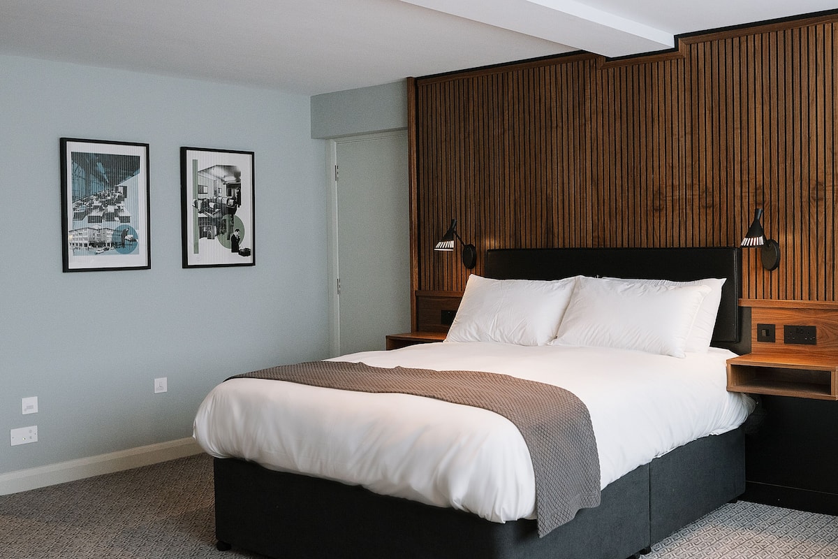 A modern bedroom with a large bed, wooden panel wall, two bedside tables, and two framed pictures on the wall.