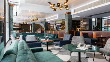 A modern lounge area with green upholstered seating, a bar with a mirrored backsplash, and a staircase leading to an upper level.
