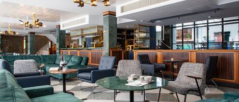 A modern lobby with green sofas, a bar area, and a staircase.