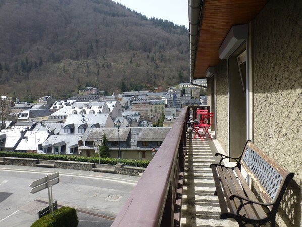 A balcony with a bench and red chairs, overlooking a town with buildings and a forested hill in the background. - Bright Apartment Maison Perce Neige, Wi-Fi, healing water   (Cauterets)