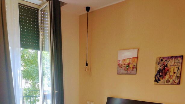 Habitación de hotel con una cama grande, una mesita de noche pequeña, una ventana con persianas y un cuadro en la pared.